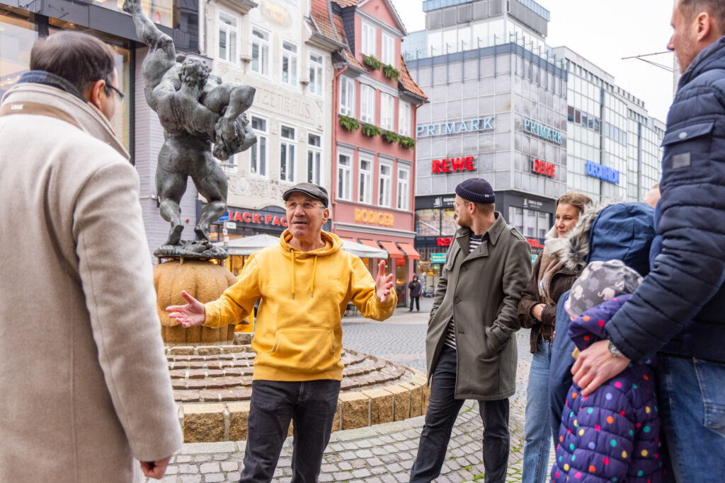 Hans-Dietrich Haacke ist mit Teilnehmern seiner Stadtführung in Braunschweig am Ringerbrunnen und erzählt fakten und Anekdoten über Braunschweig.